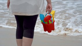 Indian woman in white shirt standing on sea shore, beach looking at waves, holding a colorful sand castle making kit toy at baga beach in goa India - Powered by Shutterstock - Get 15% off with code: PIKWIZARD15