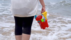 Slow motion shot Indian woman in white shirt standing on sea shore, beach looking at waves, holding a colorful sand castle making kit toy at baga beach in goa India - Powered by Shutterstock - Get 15% off with code: PIKWIZARD15