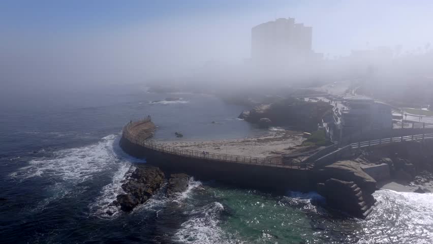 Aerial view of Childrens Pool in La Jolla during the morning with the marine layer showing a foggy low flying clouds over the coast of San Diego California with otherwise blue sky