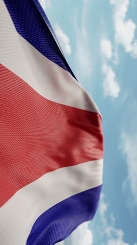 Wavy flag of Costa Rica blowing in the wind in slow motion. Waving colorful flag team symbol abstract vertical background. Blue sky with clouds. World countries flying flags concept