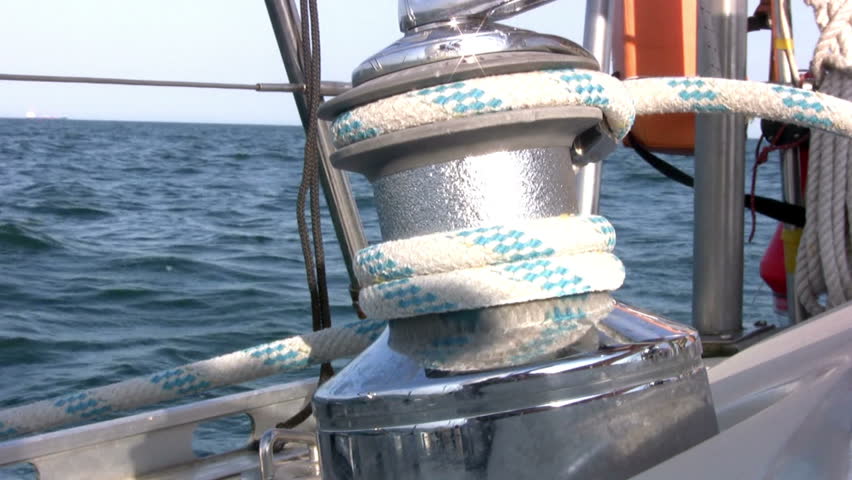 Man rotates the yacht winch and pull the halyard against the backdrop of blue