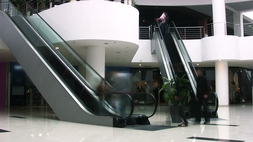 Shopping center. Two escalators. People going up and down by escalators.
