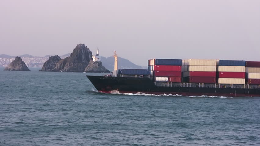 The early evening. Container ship sails to the port near lighthouse on a rock