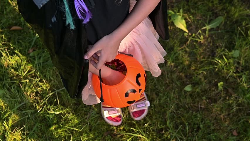 Happy Halloween day. A little cute girl in a witch costume is holding her pumpkin Jack's bucket with candy in her hand. Halloween party, kids trick or treat, close-up. Fullhd