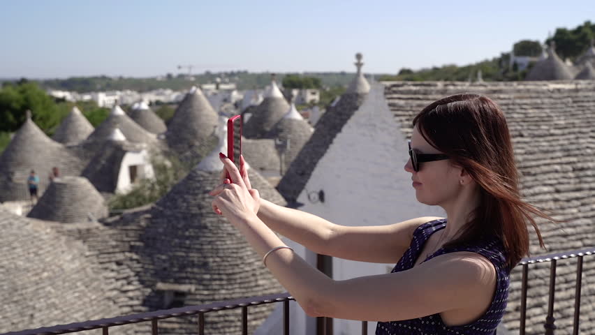 A woman takes a selfie in front of white trulli in Apulia.
