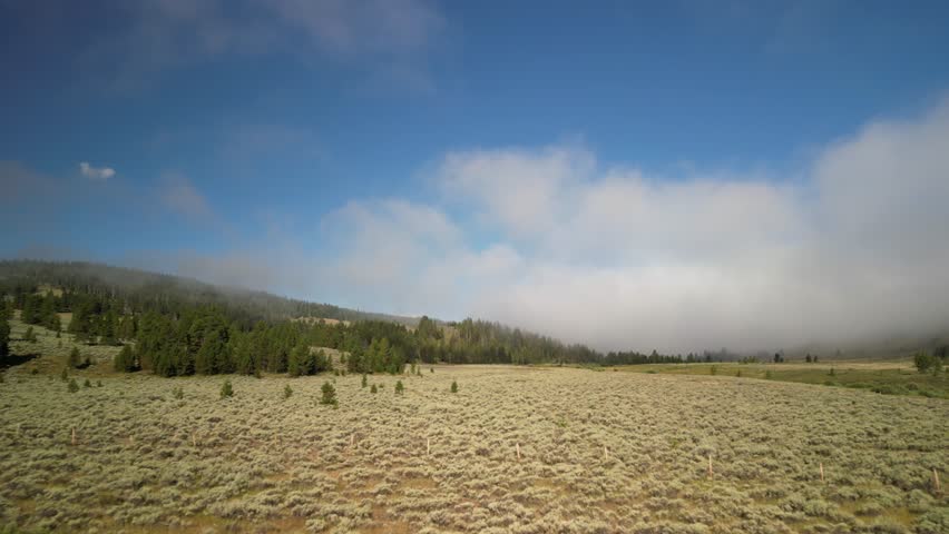 Aerial over grassy meadow in Madison Range in Montana with low clouds in summer