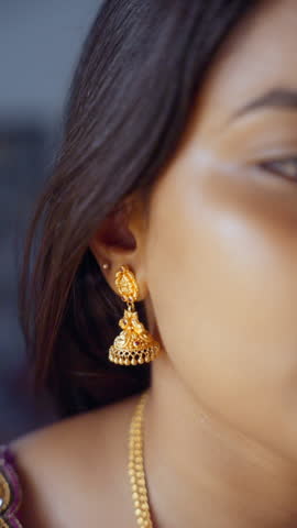 Close up of a female wearing gold earrings, smooth skin, dark hair, and Indian