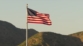 The American flag waves proudly in the mountain air, symbolizing patriotism and unity during a beautiful sunset, embodying the spirit of democracy and freedom. It is an iconic symbol of the USA - Powered by Shutterstock - Get 15% off with code: PIKWIZARD15