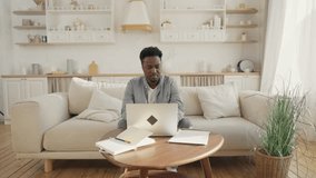 African American man working from home remotely, sitting on sofa, using laptop. Portrait of young adult freelancer man at home, workplace and home office of employee, black male person with computer - Powered by Shutterstock - Get 15% off with code: PIKWIZARD15