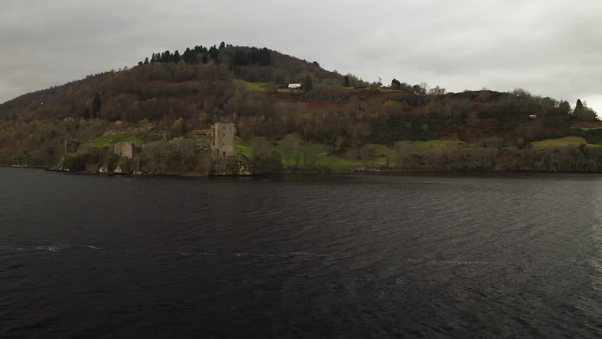 Aerial low orbit around Urquhart Castle in Loch Ness Scotland under overcast gloomy sky