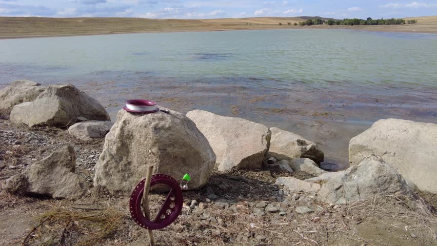 A hooked carp fishing rod with a bell attached to it, thrown into the lake for fishing.