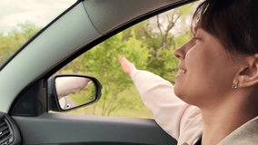 Smiling young travel woman riding car with hand waving window closeup side view. Happy relaxed female enjoy freedom road trip inside automobile with positive emotion. Summer countryside highway - Powered by Shutterstock - Get 15% off with code: PIKWIZARD15