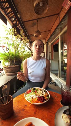 Young Hungry Pleased Woman Eating Buddha Bowl and Drink Kombucha in Restaurant. Smiling Girl Eating Fast Food and Enjoying. Thailand, Pai