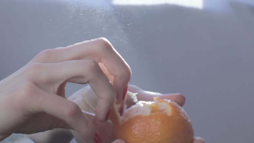 Hands of young woman peel tangerine (mandarin). Orange fruit splashes are