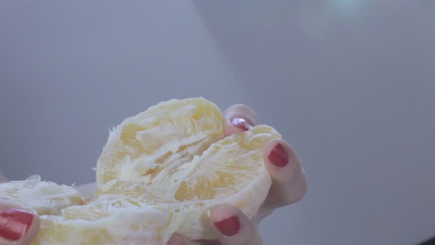 Hands of young woman tear orange apart. Orange fruit splashes are fountaining to