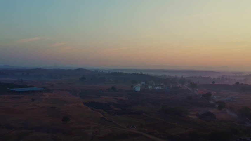 Drone ascends to clear landscape with a beautiful sunrise, against a foggy morning weather at Madhya Pradesh, India.