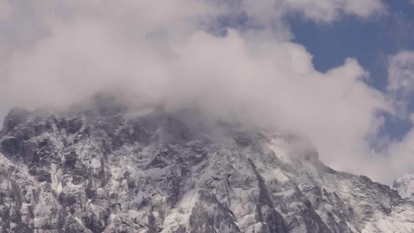 Mystic clouds flying around snowy and icy Mount Everest mountain in Nepal. Sunny day with blue sky in summer. Bottom up wide shot time lapse.