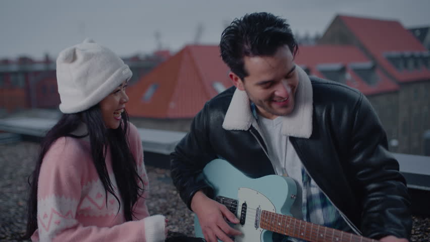 A man passionately serenades his partner with an electric guitar on a rooftop