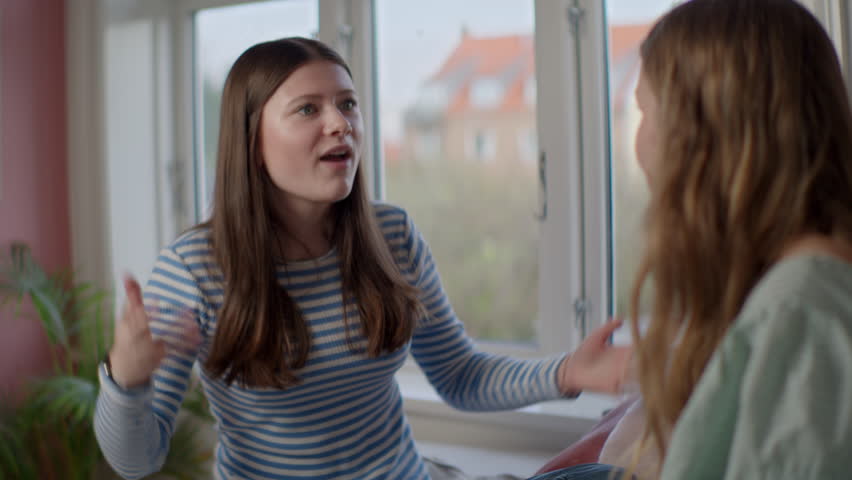 A medium shot of two teenagers in the midst of a heated argument. The girl in the striped top passionately explains her side with an emotional expression, as they engage in an intense discussion