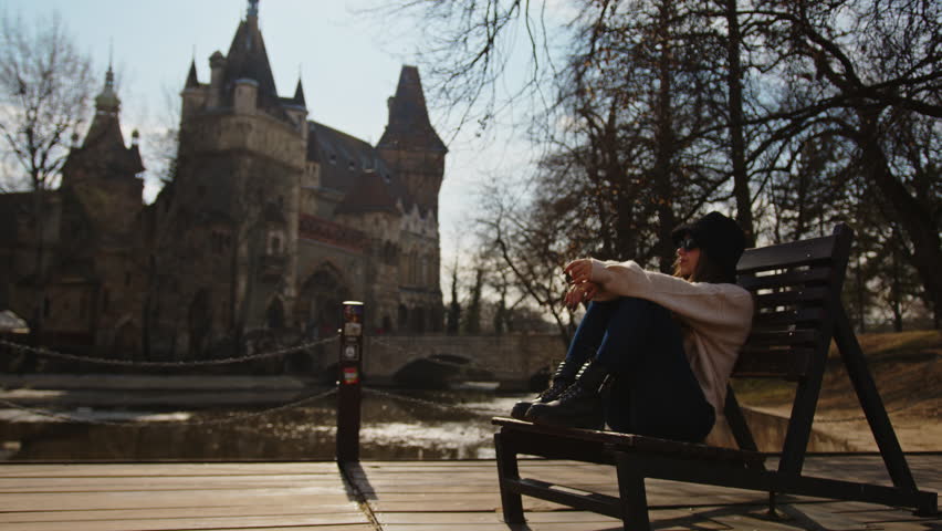 Beatiful Young Girl Enjoying Weekend Sitted In A Bench In Vajdahunyad Castle Garden in Budapest, Hungary