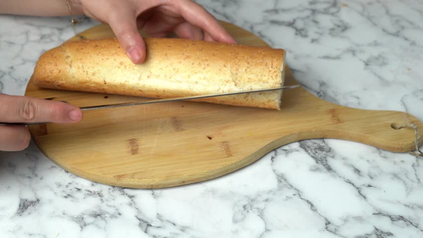 Girl cutting bread in half with sharp knife on wooden board in kitchen