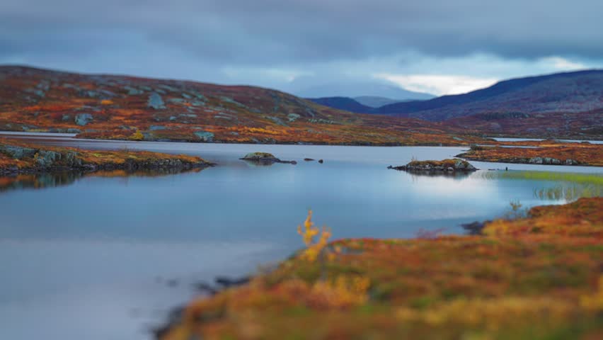 A shallow lake in the autumn tundra surrounded by the colourful autumn landscape. Heavy clouds cover the sky. Parallax video.