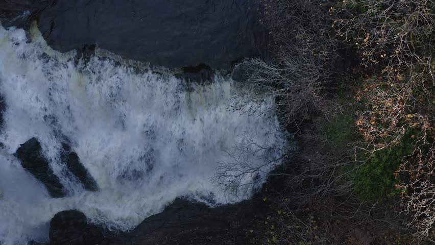 Drone overview of rushing water down waterfall in Isle of Skye Scotland with sun flare