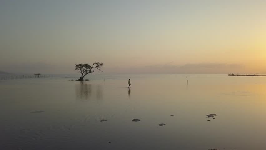 beautiful sunset above the ocean surface and a man walking on the water. Aerial view of sea surface during the dusk. Drone flies over the water straight to horizon.