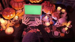 Top view, skeleton hands typing on keyboard laptop with green chroma key screen next to Halloween attributes pumpkins, candles and skull. Creepy horror Happy Halloween party, background. - Powered by Shutterstock - Get 15% off with code: PIKWIZARD15