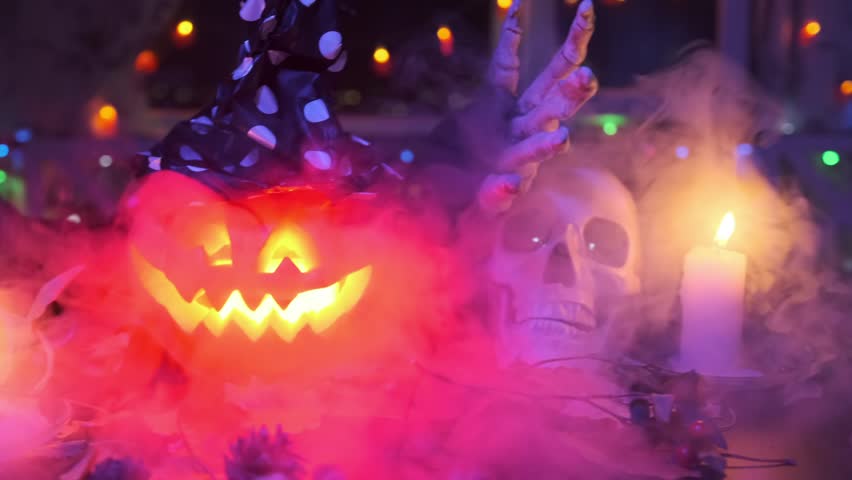 Halloween pumpkin in a witch hat calls to join the party slow waves bony hand against the backdrop of eerie fog and flickering candles. Close up.