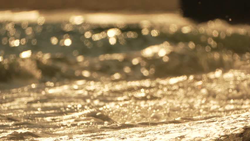 Golden sunset on the beach. Foamy waves rolling towards golden sand beach under low warm sun light. Slow motion. Nobody. Holiday recreation concept. Abstract nautical summer ocean sunset nature.