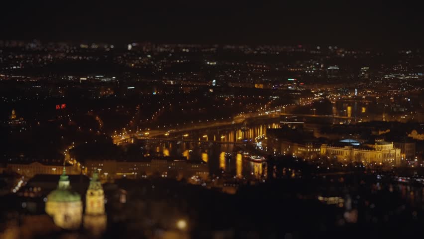 Prague at night - dim street lights on the quay and traffic on the streets and bridges. Aerial view, tilt-shift.