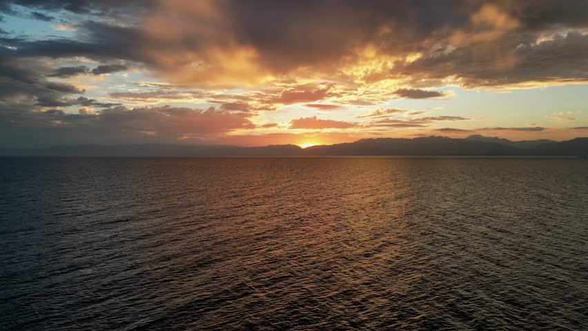 Aerial over ocean during vivid sunset over horizon with orange and yellow clouds