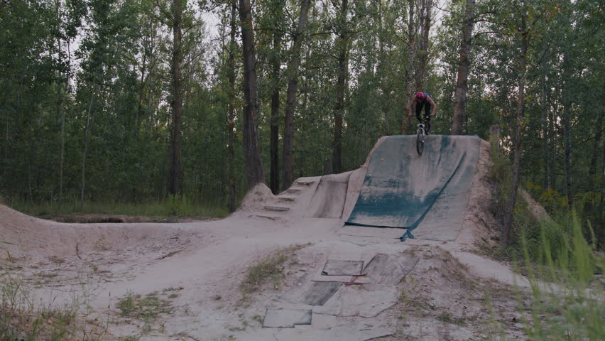 Muscular man in sportswear riding down high sandy hill and rising in air while taking hand off steering wheel. Ambitious dirt jumper practicing dangerous stunt alone in country territory.