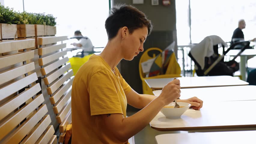 Dinner and meal with organic products concept. Young caucasian woman with short hair eating delicious red tomato soup in cafe or restaurant. Vegetarian cuisine and healthy vegetable diet. Side view