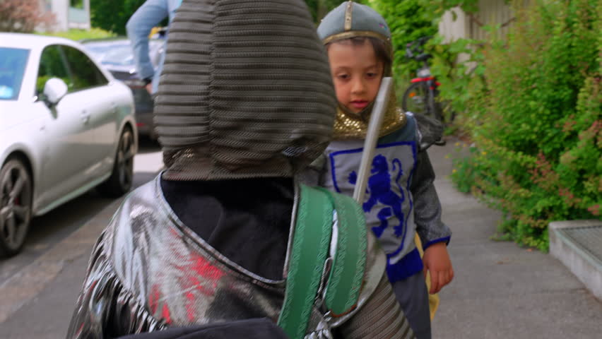 Children dressed as knights, one in a silver helmet holding a sword, playing on the street. the spirit of childhood imagination and adventure during a playful interaction