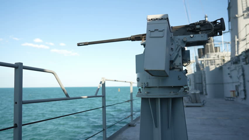 Color image of an automated machine gun on the deck of a military ship, at sea.