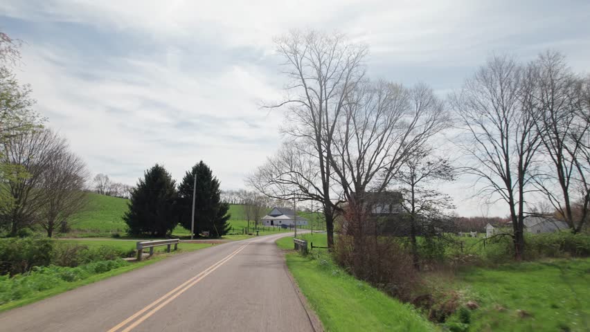 Driving around small town America in Ohio countryside, moving past wood buildings, old barns, farm land, crops, trees, and large fields in conservative rural area outside Columbus and Danville, OH 