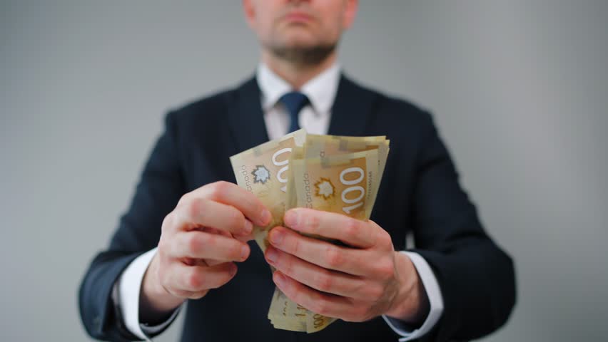 Formally dressed man is counting Canadian Dollar bills, close-up.