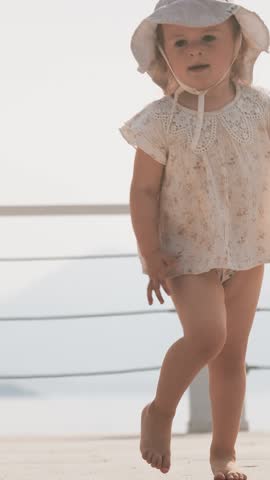 Little baby girl runs on the seaside pier on a summer day, slow motion, vertical video