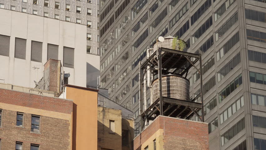 Close-up of a rooftop water tank with a background of towering office buildings, capturing a mix of industrial and corporate architecture in NYC.