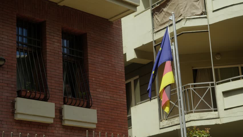 Flags of Germany and the European Union are displayed in front of the German Embassy in Tbilisi, Georgia, against the backdrop of private residences. Slow motion