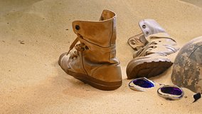 military helmet, a pair of worn combat boots, and a pair of broken sunglasses, partially buried in the sand. The arrangement suggests a narrative of someone having been in this harsh environment - Powered by Shutterstock - Get 15% off with code: PIKWIZARD15