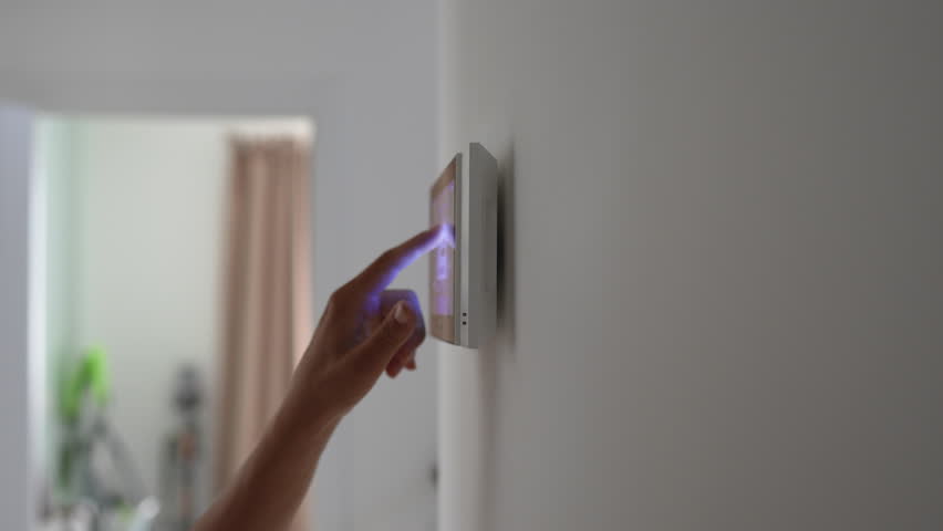 Closeup hand using smart home touch screen with connected appliances device on wall. Setting, checking energy security heating system on digital control in apartment. Home automation monitoring.
