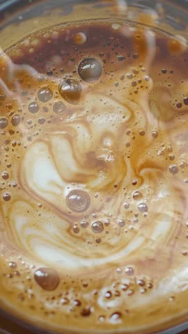 Close-up of a latte or cappuccino. Coffee texture and coffee beans spreading the drink in swirling foam with dark brown coffee scattered throughout the foam.