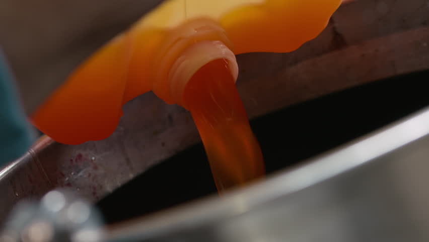 Closeup of orange liquid pouring from canister in worker hands into tank at cider production factory