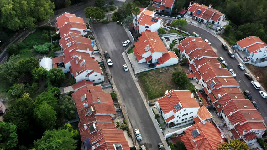 Aerial footage residential neighborhood in suburbs of Sintra Portugal featuring typical one-story and two-story houses adjacent to lush forest. Drone captures the peaceful ambiance 