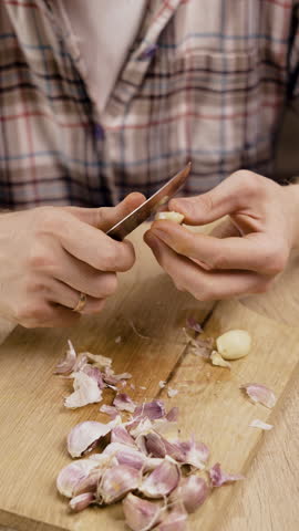 man peeling fresh garlic on wooden cutting board in kitchen