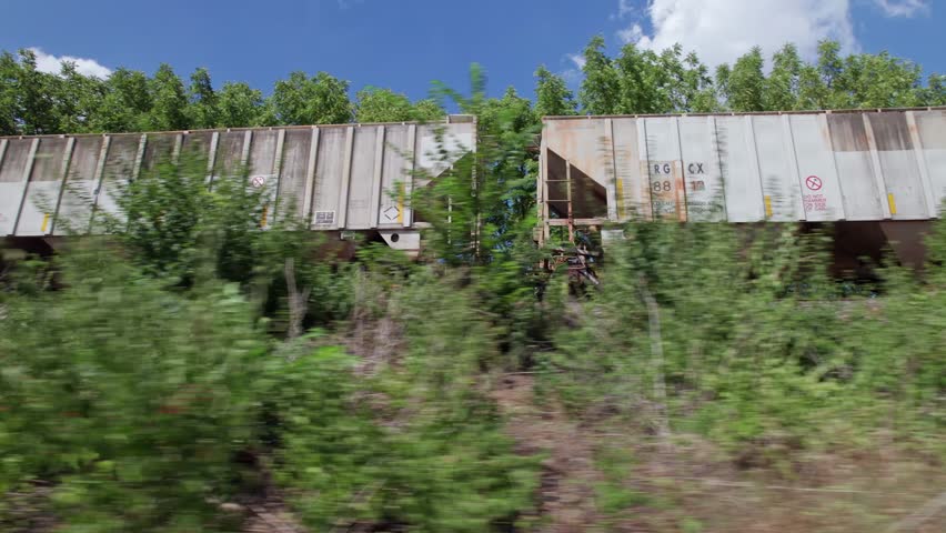 Driving alongside moving freight train and industrial railroad tracks to push industry and supply forward in the midwest part of the United States