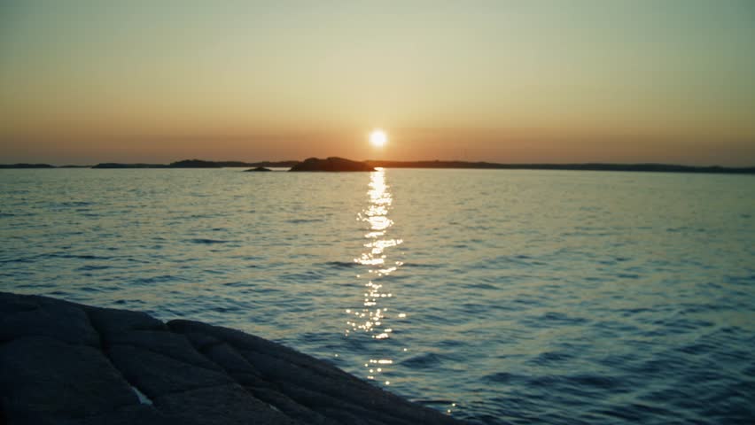 The sun sets over the rugged coastline of Nova Scotia, casting a dramatic orange glow on the crashing waves and rocky shore. Canada. View beautiful evening sunset in sky over sea.